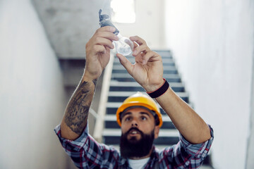 An electrician screwing the light bulb at his workplace. - Powered by Adobe