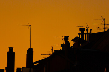 Silhouettes of antennas, chimneys and roofs under a sunset sky