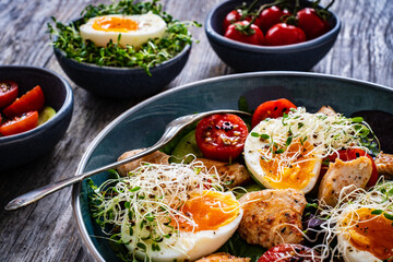 Chicken salad  - chicken nuggets, hard boiled eggs, cherry tomatoes, lettuce, cucumber and sprouts on wooden table	