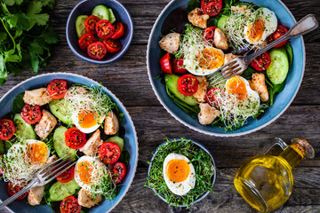 Chicken salad  - chicken nuggets, hard boiled eggs, cherry tomatoes, lettuce, cucumber and sprouts on wooden table	