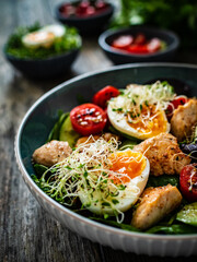 Chicken salad  - chicken nuggets, hard boiled eggs, cherry tomatoes, lettuce, cucumber and sprouts on wooden table	