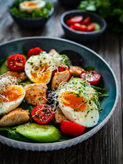 Chicken salad  - chicken nuggets, hard boiled eggs, cherry tomatoes, lettuce, cucumber and sprouts on wooden table	