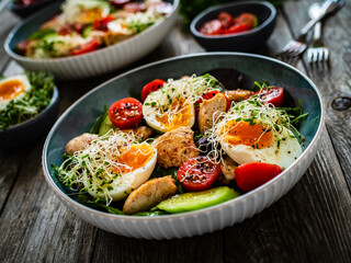 Chicken salad  - chicken nuggets, hard boiled eggs, cherry tomatoes, lettuce, cucumber and sprouts on wooden table	