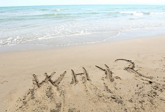 text WHY with question mark that was written in the sand by the sea