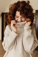 Charming cute lady with curls wearing knitted pullover is laughing and looking down with closed...