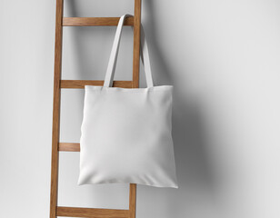 white plain cotton canvas tote bag hanging on wooden ladder against white isolated background. 