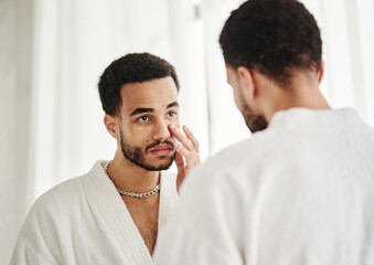 Young handsome metrosexual looking at mirror and applying eye patches on his face