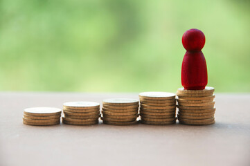 Red wooden doll standing on stack of gold coins. Business concept