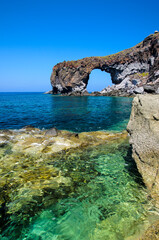 Natural volcanic arch formed from lava on the crystal clear tyrrhenian sea in Punta Perciato,...