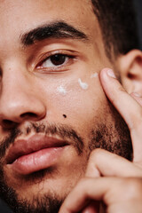 Close-up of young mixed race man applying cream on his face