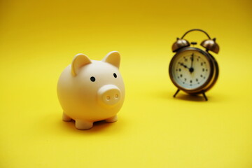 Piggy bank and alarm clock with space copy on yellow background