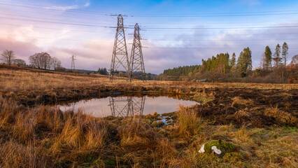 Electricity pylons overlooking a new artificial farm pond, at sunset in winter