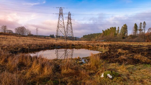 Electricity pylons overlooking a new artificial farm pond, at sunset in winter