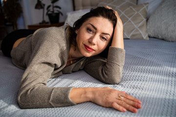 Beautiful middle age woman rest on bed look at the camera. Successful middle aged woman smiling at home.