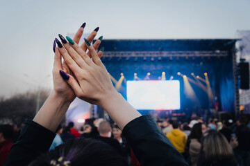 woman claps his hands at musical concert in a crowd of people. clapping crowd at singer's concert. smoke, applause and hands in soft focus, abstract background