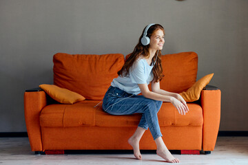 Obraz premium pretty woman on the orange sofa listening to music with headphones technologies