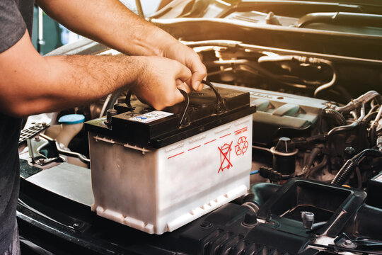 A auto mechanic carries a replacement car battery for car electrical maintenance