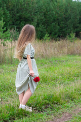Young blond long haired woman with red blossoming dahlia flower in hand is standing on road with...
