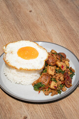 Closed up Famous Thai food padkaprow.  A plate of delicious Stir fried  fresh holy basil mix pork minced and sausage with toped rice fried egg on wooden background.