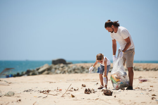Volunteers father and little daughter cleaning beach from trash left by tourists