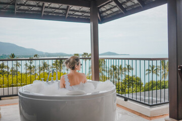 Young woman enjoy bathing in a bathtub with soap bubbles, Luxury jacuzzi suite for relaxation on balcony with landscape of sea view, Samui, Thailand - obrazy, fototapety, plakaty