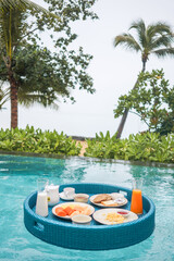 Floating breakfast in swimming pool with sea view. Healthy breafast served on the table relaxing in calm pool water, by tropical resort pool, summer beach luxury lifestyle