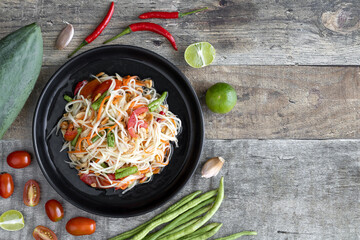 Green papaya salad with tomatoes, peanuts, Chinese beans, chili. Traditional Thai papaya salad on a wooden table, top view, copy space.