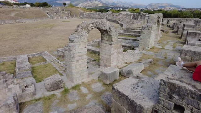 Tourist woman on top of the Salona ruins of the Ancient Roman Amphitheatre of Dalmatia in Croatia. Historic Roman town ruins in Flavian architectural style.