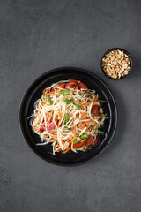Spicy papaya salad in a black plate on a gray background, top view, copy space. Thai food top view.