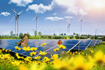 Solar panel with wind turbines against mountains and sky as background and flowers in a blurred...