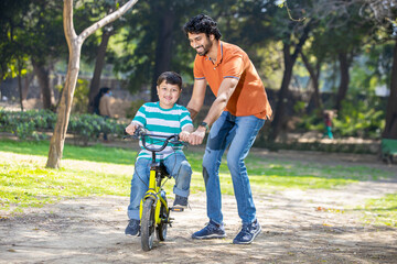 Young Indian father help on learn to ride a bicycle at summer park, Kid outdoor sport activity. 