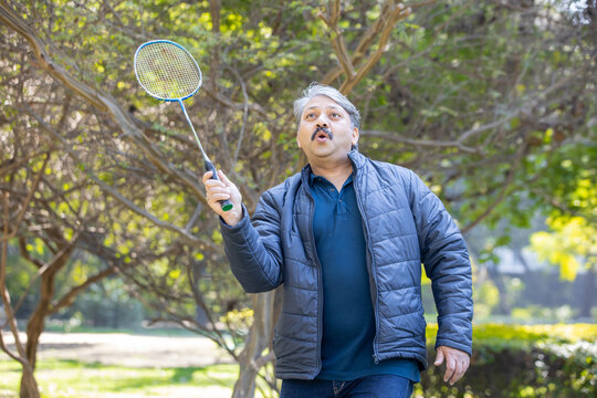 Senior Indian Man Playing Badminton In The Park. Urban Asian Sporty Elderly Male Having Fun Outdoor Sports And Game Activity Concept. Copy Space