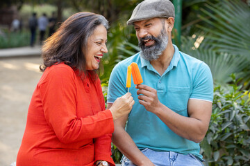 Happy indian senior couple enjoy ice lolly or ice cream outdoor,  mature people enjoy retirement...