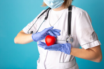 Hands in medical gloves holding a red heart shape model on blue background. Cardiology, organ donation or Healthy heart concept