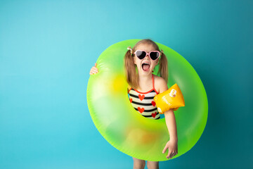 Funny happy child in bright swimsuit and sun glasses smiling and holding a swimming ring on colored...