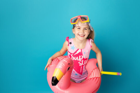 Happy little child girl with swimming mask and snorkel smiling and standing above blue background. Summer and vacation concept