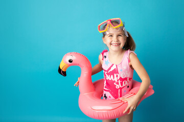 Happy little child girl with swimming mask and swimming ring standing above blue background. Summer...