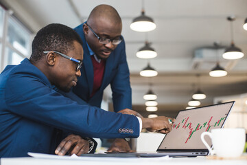 Two African American business partners are working on a laptop studying stock market charts and technical analysis. Training in investment and analysis of macroeconomic and financial indicators