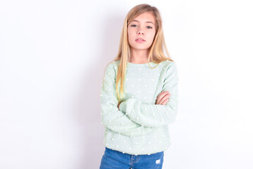 Serious pensive little caucasian kid girl wearing fashion sweater over blue background feel like cool confident entrepreneur cross hands.