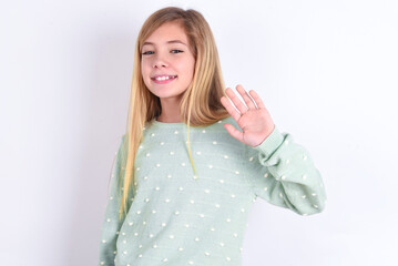 little caucasian kid girl wearing fashion sweater over blue background Waiving saying hello happy and smiling, friendly welcome gesture.