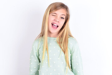 little caucasian kid girl wearing fashion sweater over blue background winking looking at the...