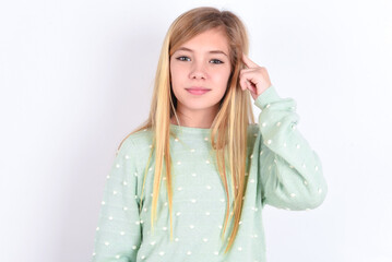 little caucasian kid girl wearing fashion sweater over blue background tries to memorize something,...