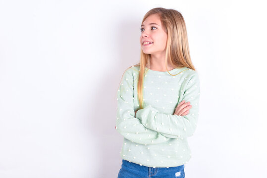 Dreamy rest relaxed little caucasian kid girl wearing fashion sweater over blue background crossing arms, looks good copyspace