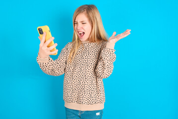 Angry little caucasian kid girl wearing animal print sweater over blue background  screaming on the...