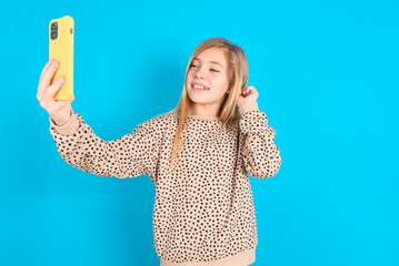 little caucasian kid girl wearing animal print sweater over blue background  smiling and taking a...