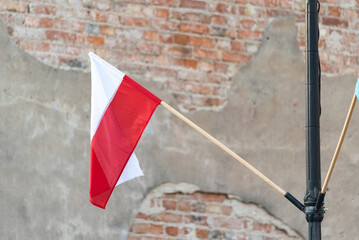 A small Polish flag on a blurry background of bricks with peeling plaster. Red and white flag. Polish national symbol and colors.