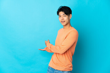 Young Chinese man isolated on blue background extending hands to the side for inviting to come