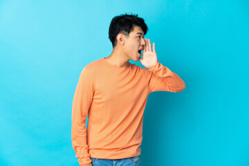 Young Chinese man isolated on blue background shouting with mouth wide open to the side
