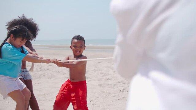 A group of children having fun playing tug of war on the beach.