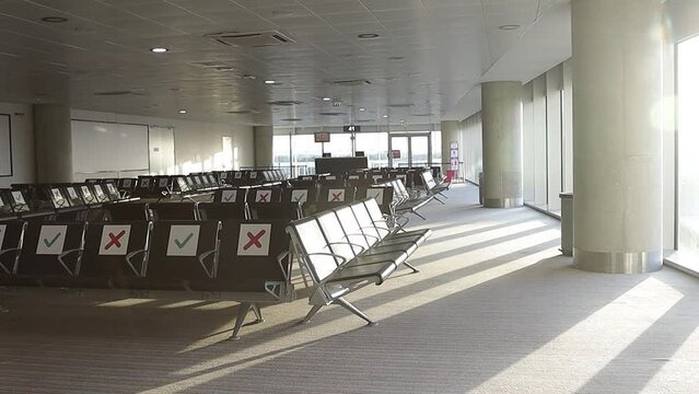 Airport during the Covid-19 pandemic. The rising sun in the morning illuminates the empty departure and waiting area from a chair with special social distancing signs